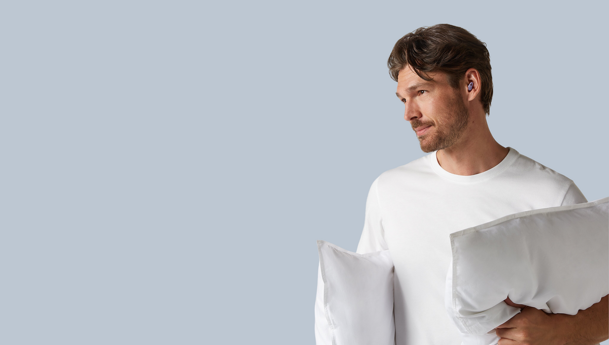 A Hears Sleep customer wearing earplugs and holding pillows